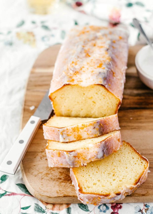 wooden board with sliced loaf cake on top, cake glazed with sugar