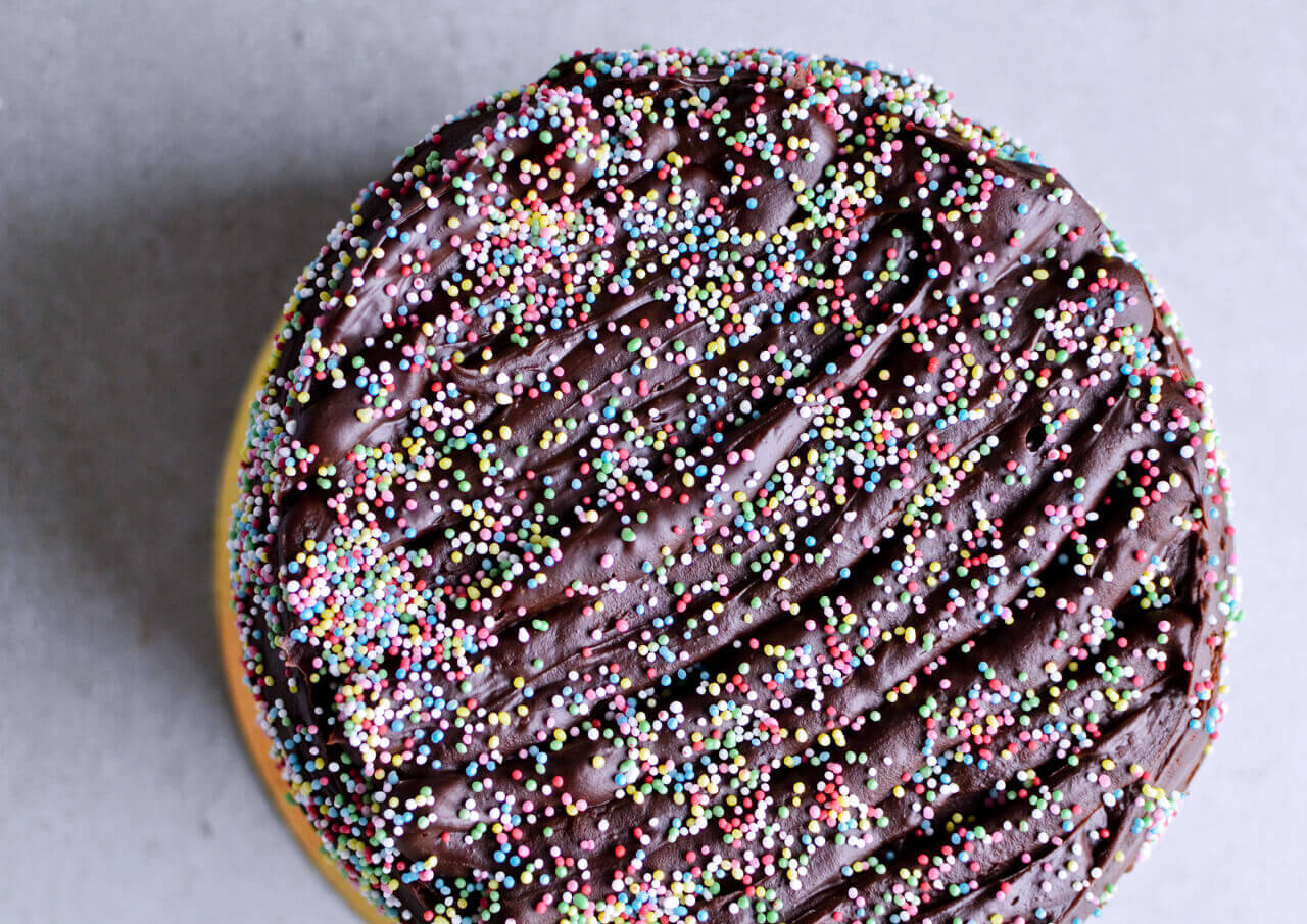 Recipe for Chocolate lover's triple chocolate ganache layer cake, every chocoholic's dream come true! Made with coffee, rich bittersweet chocolate and cream, but no butter, this chocolate cake is smooth and addicting! Topped with sprinkles and flowers, to make it super pretty. | sugarsalted.com