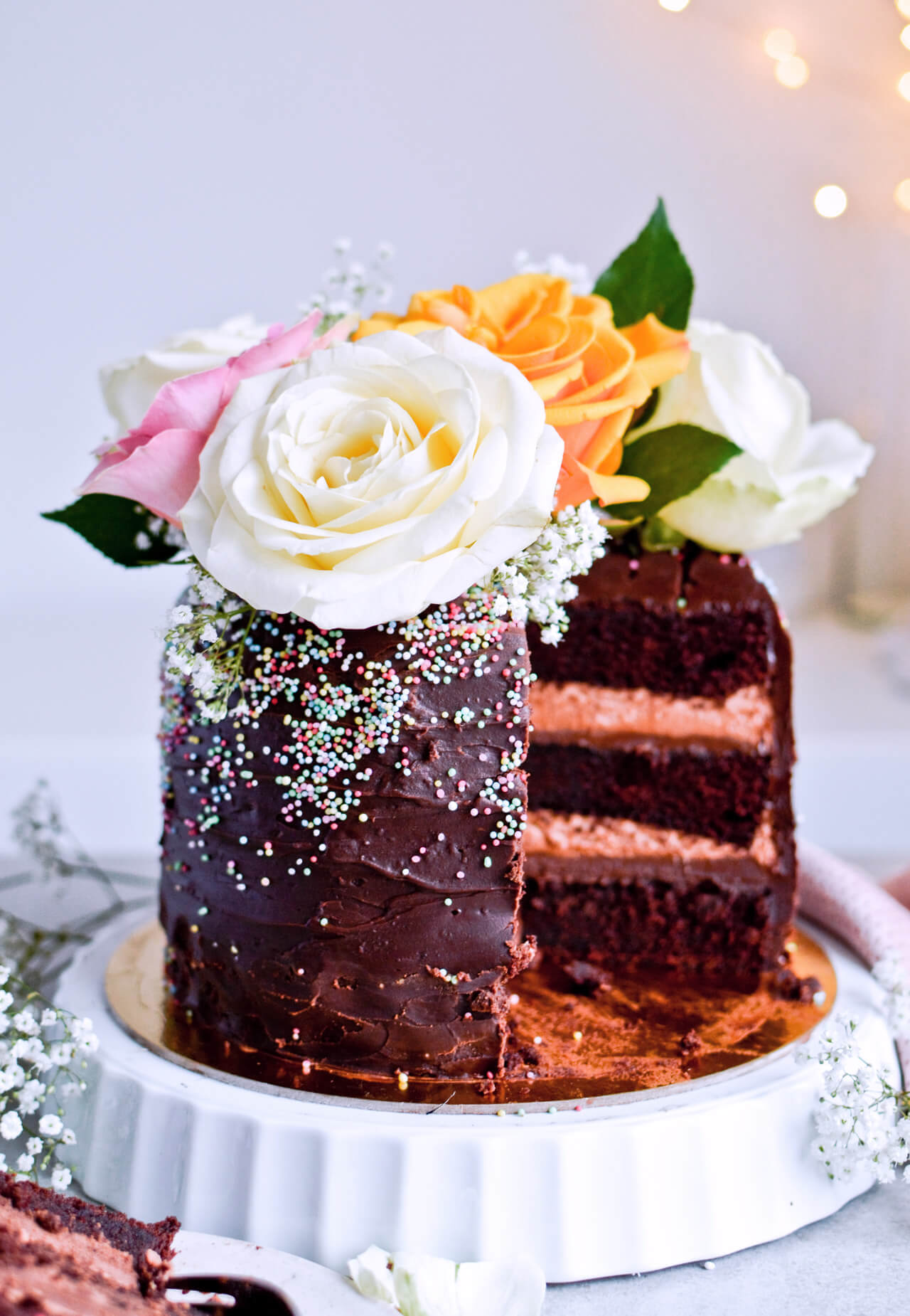 Recipe for Chocolate lover's triple chocolate ganache layer cake, every chocoholic's dream come true! Made with coffee, rich bittersweet chocolate and cream, but no butter, this chocolate cake is smooth and addicting! Topped with sprinkles and flowers, to make it super pretty. | sugarsalted.com