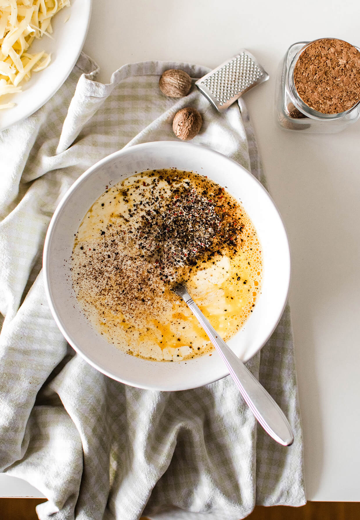kitchen towel with bowl and quiche mixture, eggs, cheese and raw nutmeg