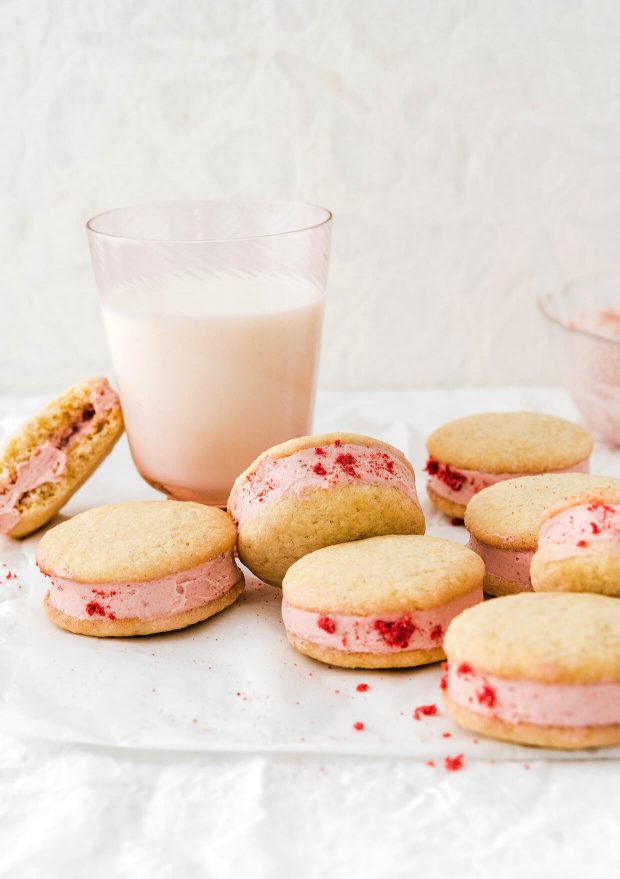 lemon strawberry cheesecake sandwich cookies scattered on table with glass of milk