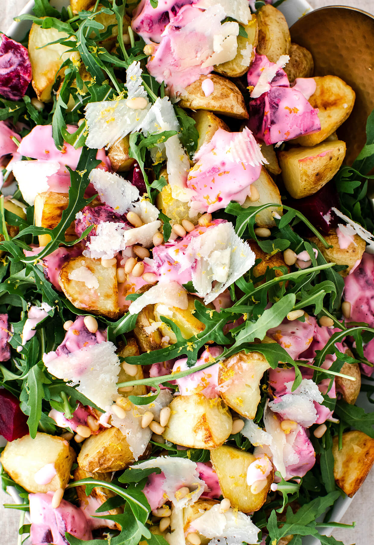 close up of roasted potato salad with beets, arugula, cheese shavings, pine nuts