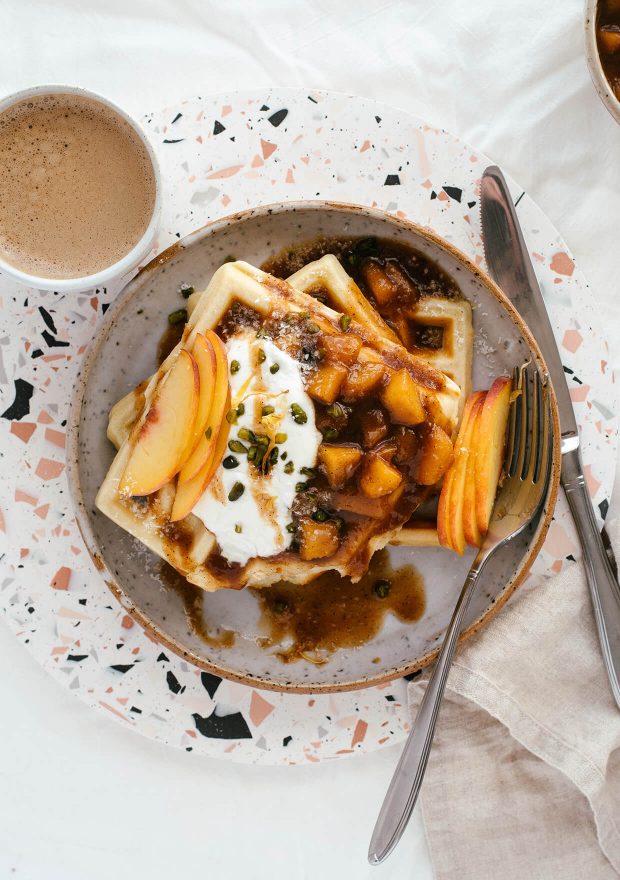 cinnamon maple peach sauce waffles with yogurt, served on plate with a cup of coffee on terrazzo board