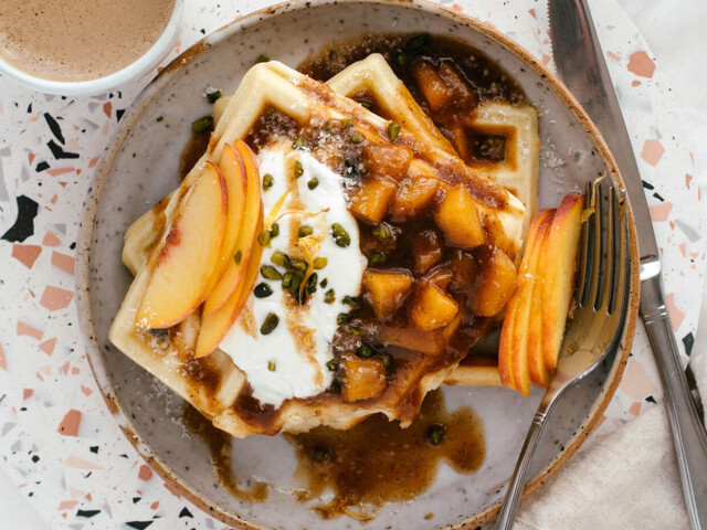 cinnamon maple peach sauce waffles with yogurt, served on plate with a cup of coffee on terrazzo board