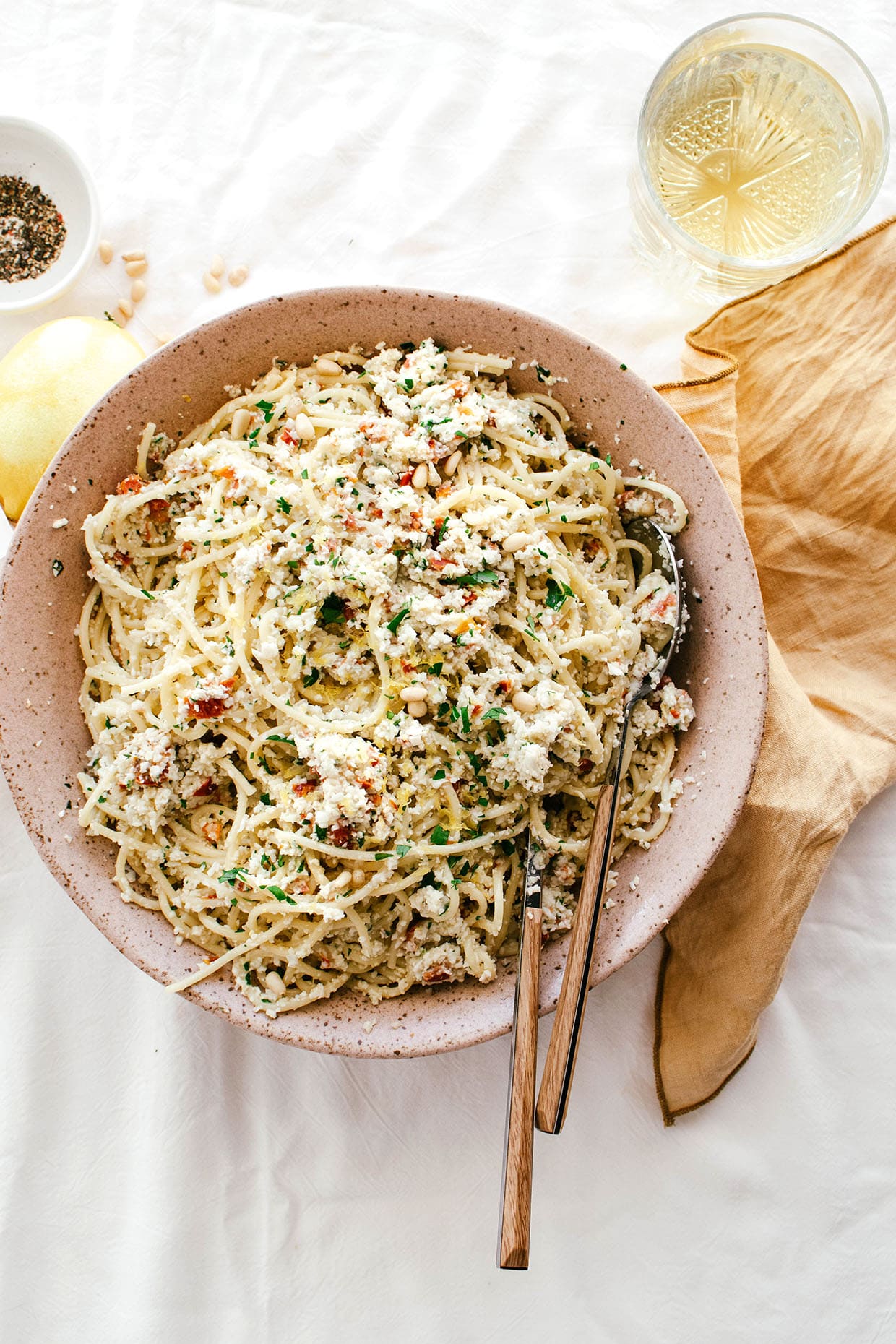 bowl of spaghetti with cauliflower pesto, wine, pepper and lemon on the side