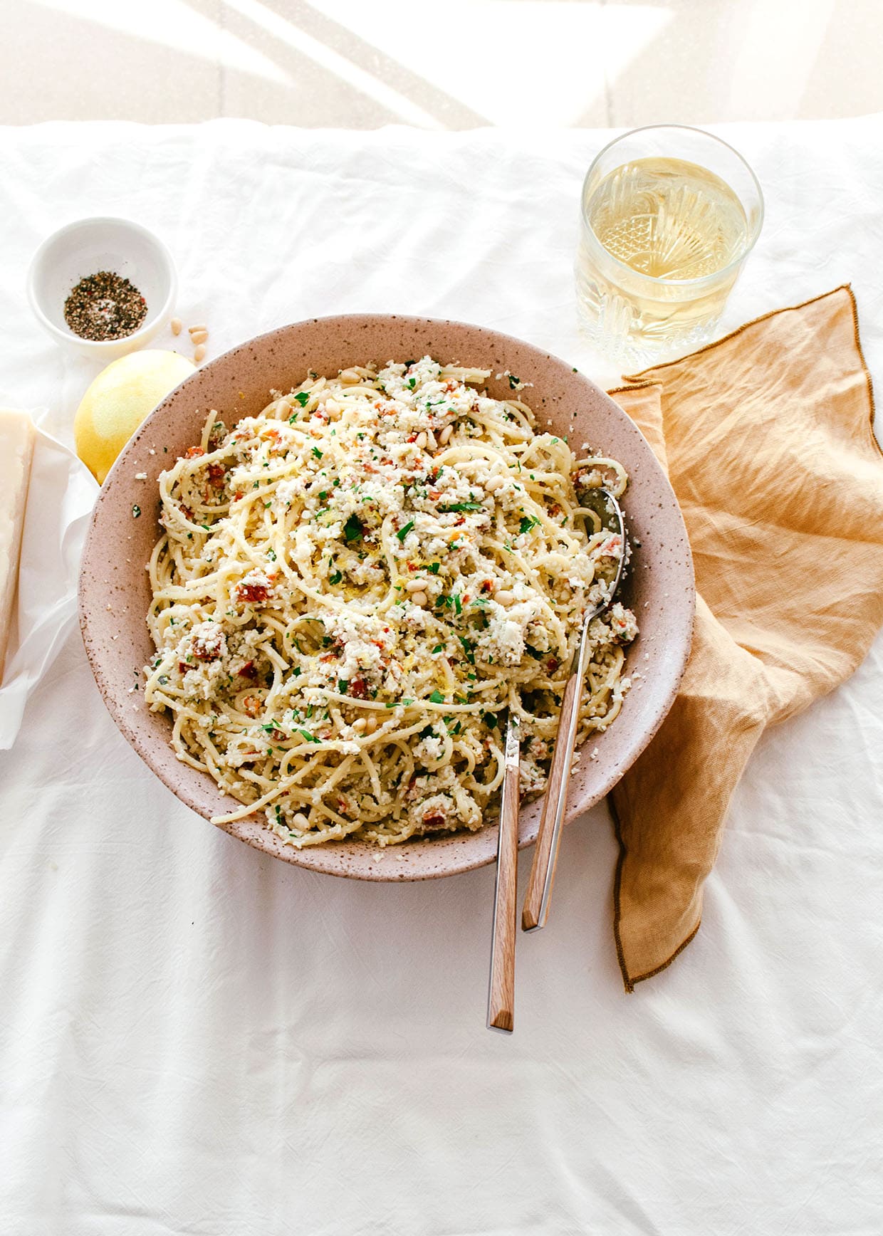 sunlit table with large bowl serving of spaghetti with cauliflower pesto, cheese, pepper, lemon and glass of wine