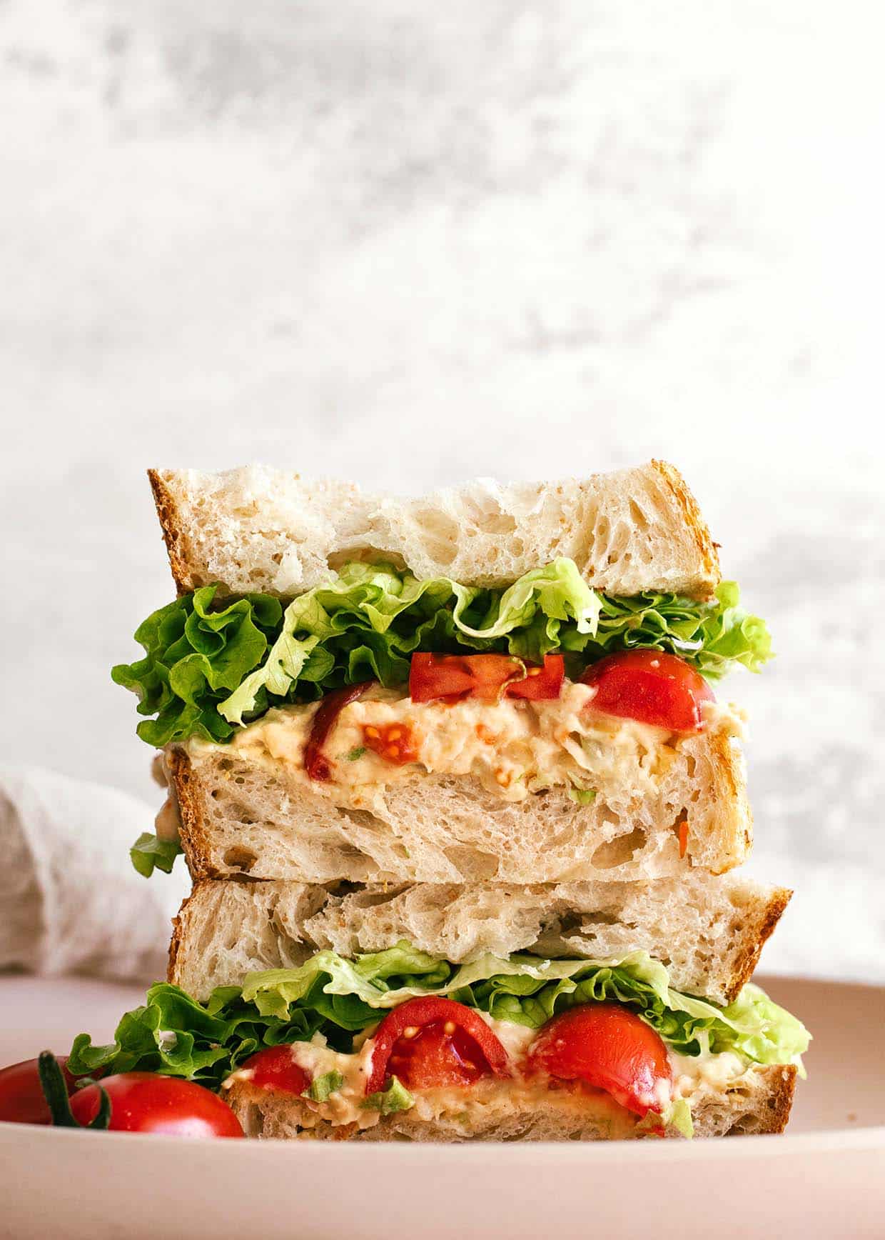 stacked chickpea tuna sandwich with lettuce, tomatoes, bread