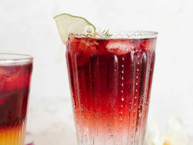 two-toned cocktail of red wine served in glass with slice of lime