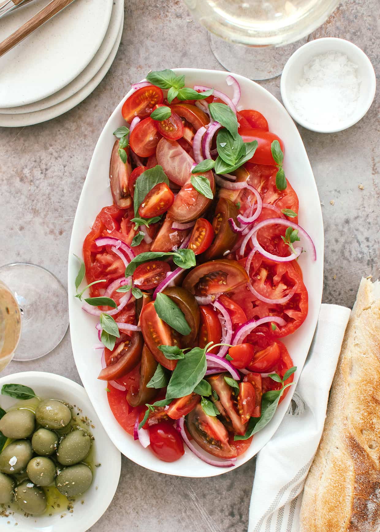 sliced tomato salad served on a platt with red onions and basil scattered on the top