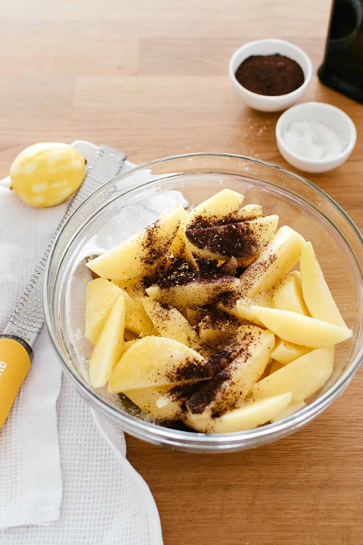raw potato wedges in a bowl, sprinkled with herbs and lemon