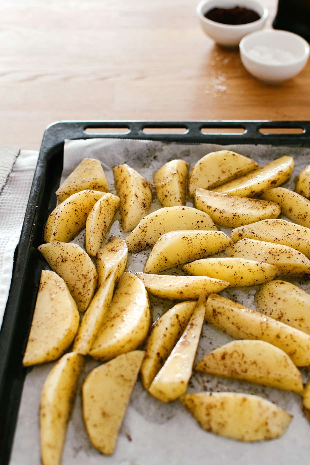 raw potatoes sliced into wedges that are arranged on a baking tray
