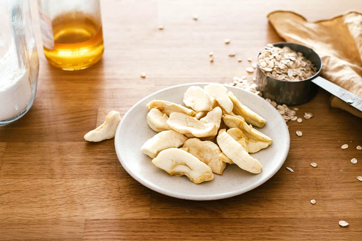 wood counter with a plate of dried apple wedges, cup of oats, jar of honey and jar of flour