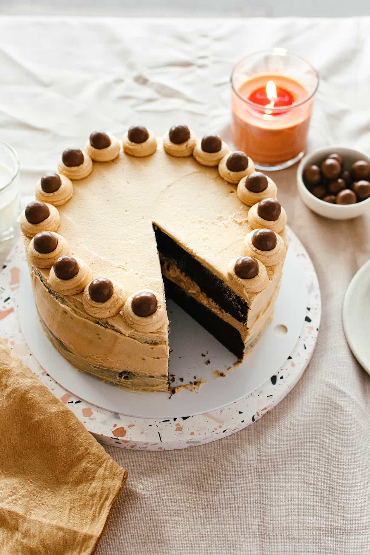 side view of beige peanut butter layer cake topped with chocolate malt balls