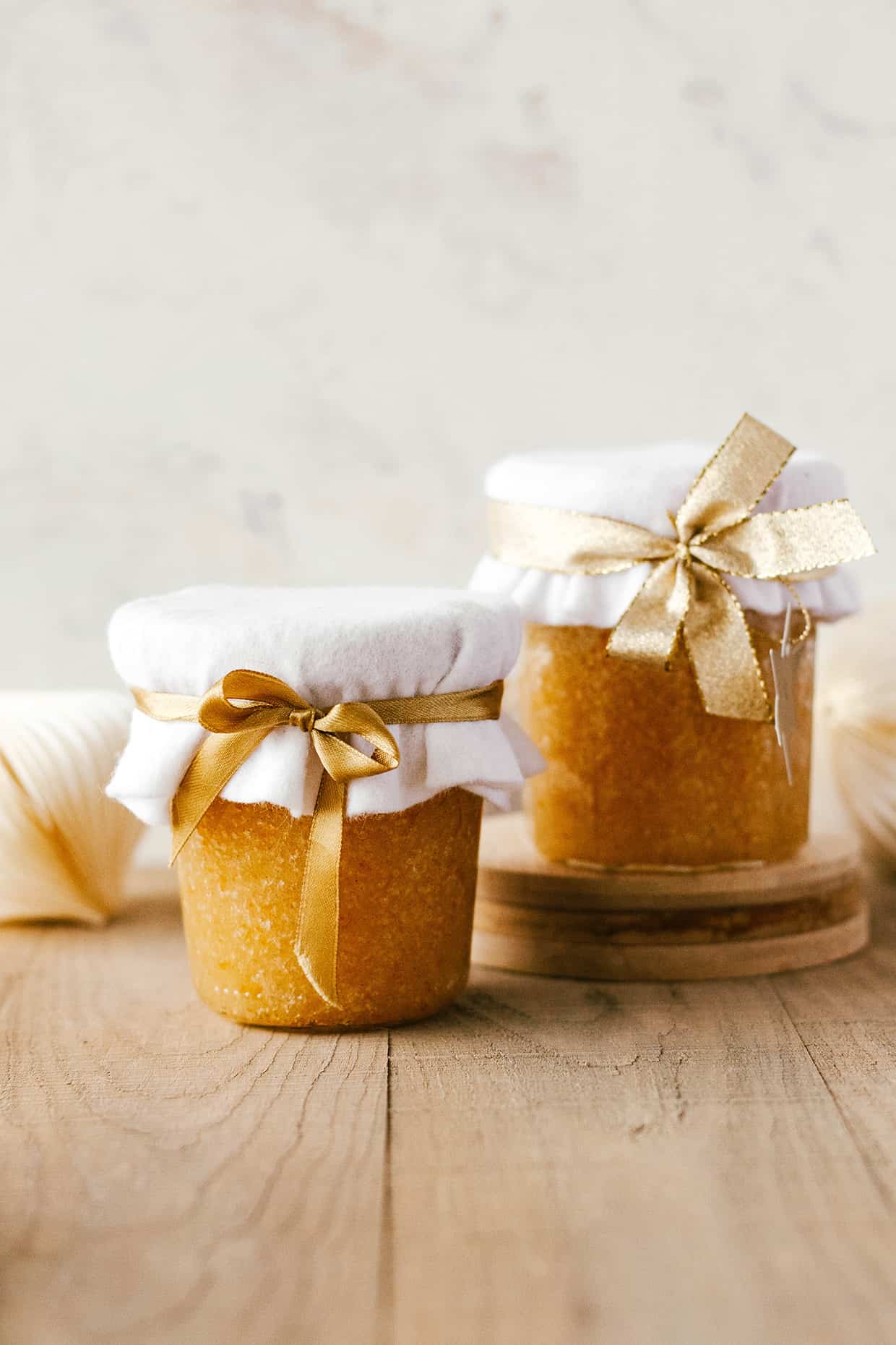two glass jars of orange sugar scrub wrapped with golden ribbon