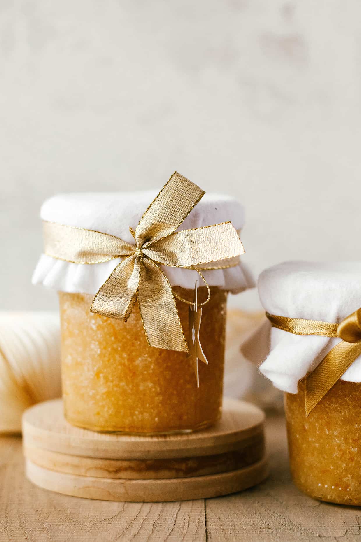 orange sugar body scrub placed in a glass jar with white fabric on top and gold ribbon wrapped around it
