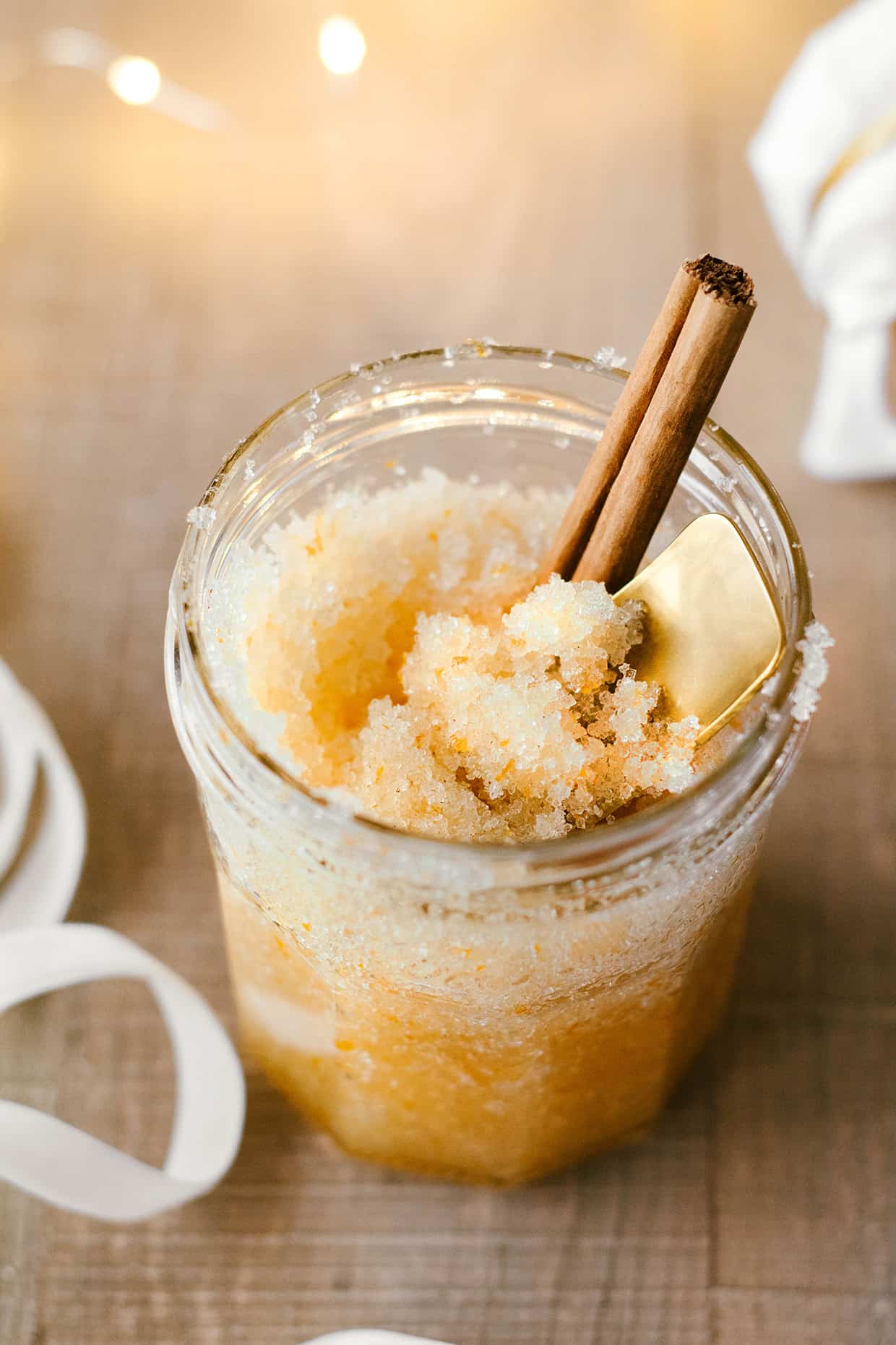 Cinnamon orange sugar scrub in a glass jar with gold scoop and cinnamon stick