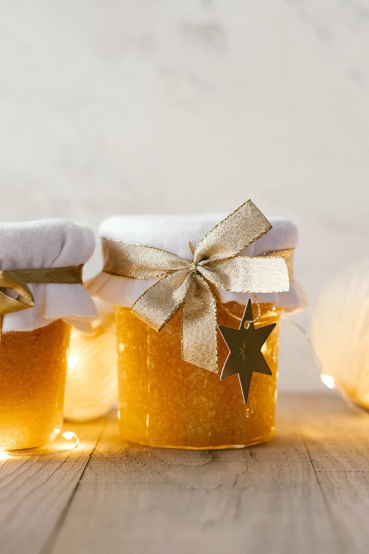 glass jar of body scrub placed on a wood table with string lights in the background