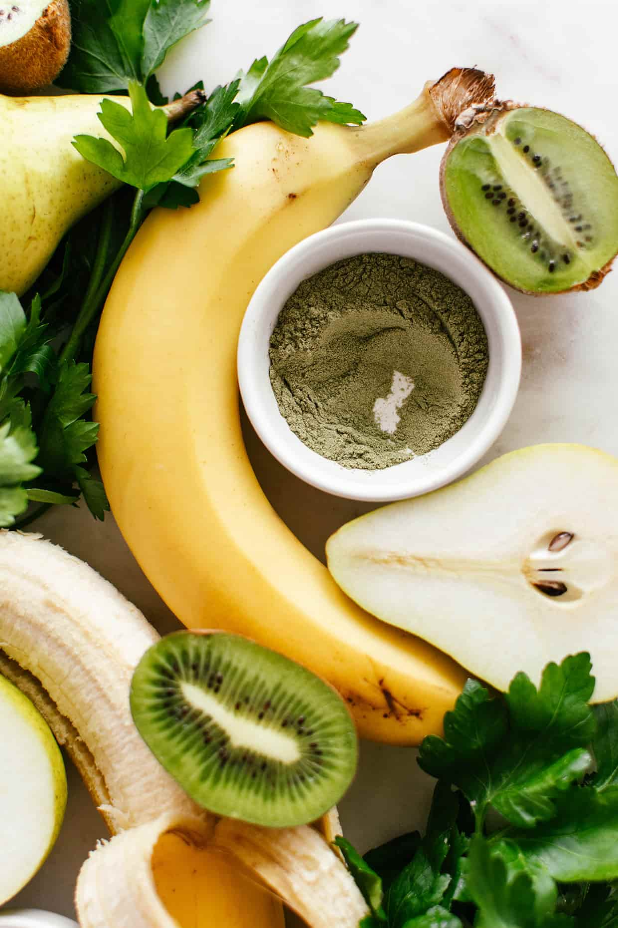 a close view of fruit sliced on a board, unpeeled banana and bowl of barley grass powder