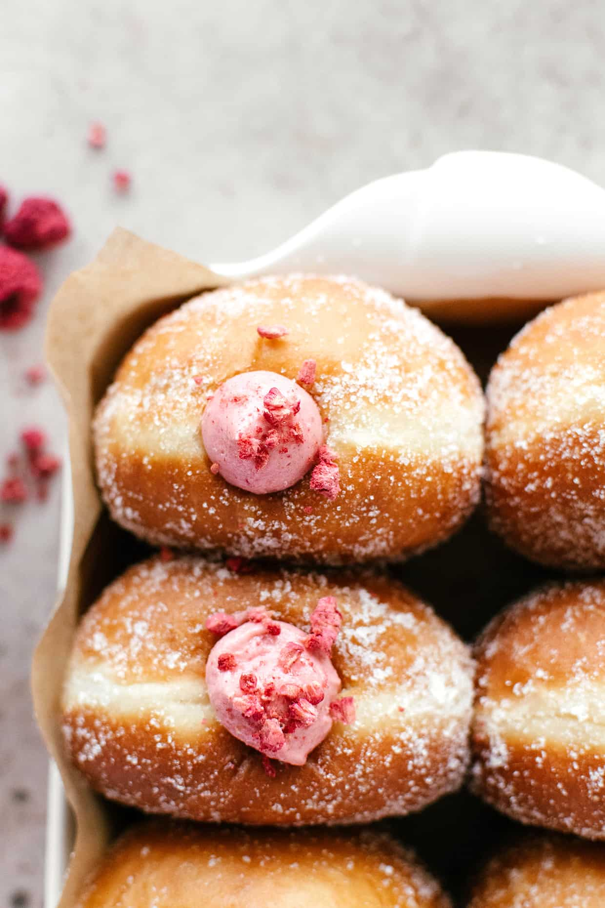 close view of a puffy golden brown doughnut with pink raspberry filling peaking out