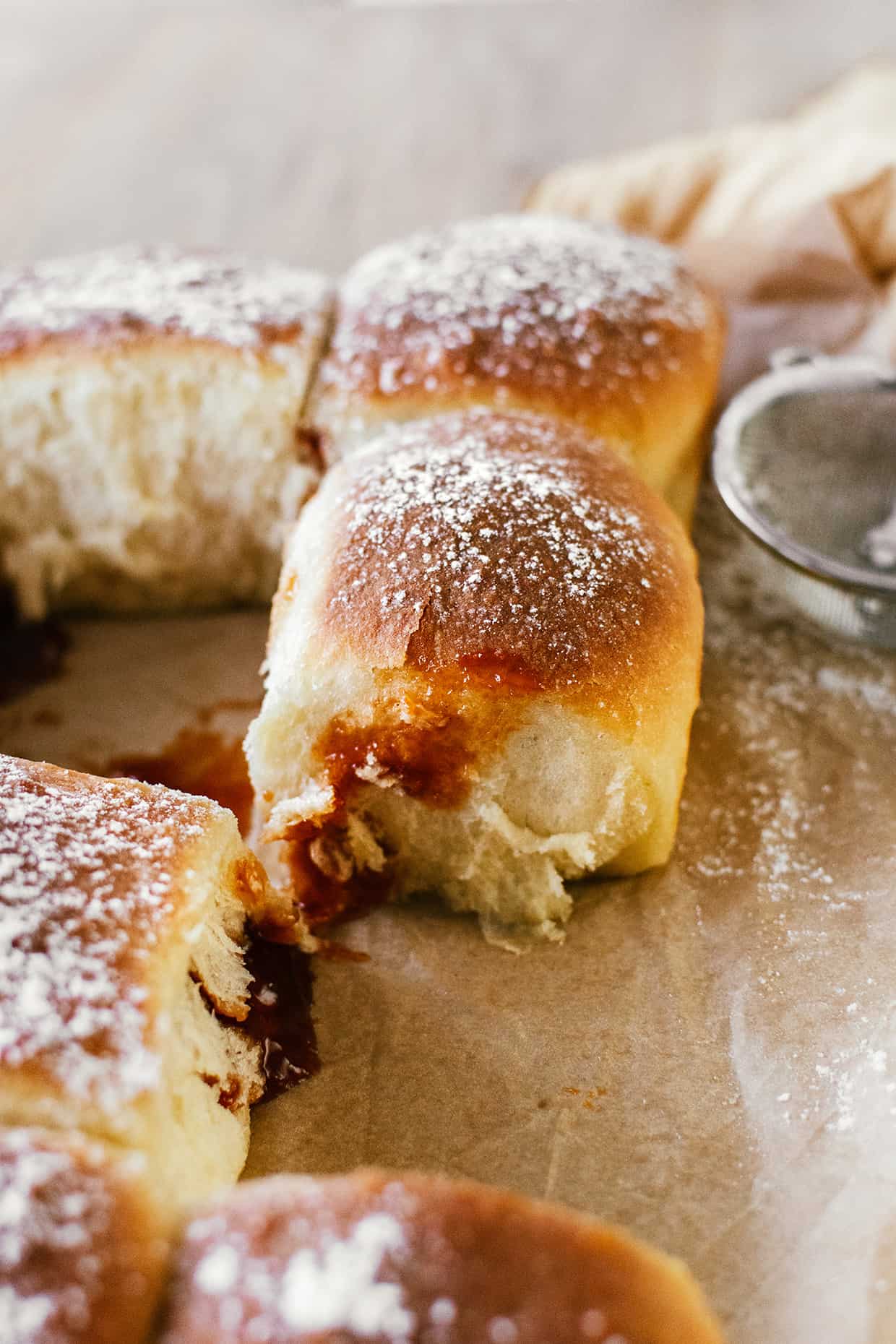 Close view of a baked bread roll, sprinkled with sugar and with jam dripping down in the front.