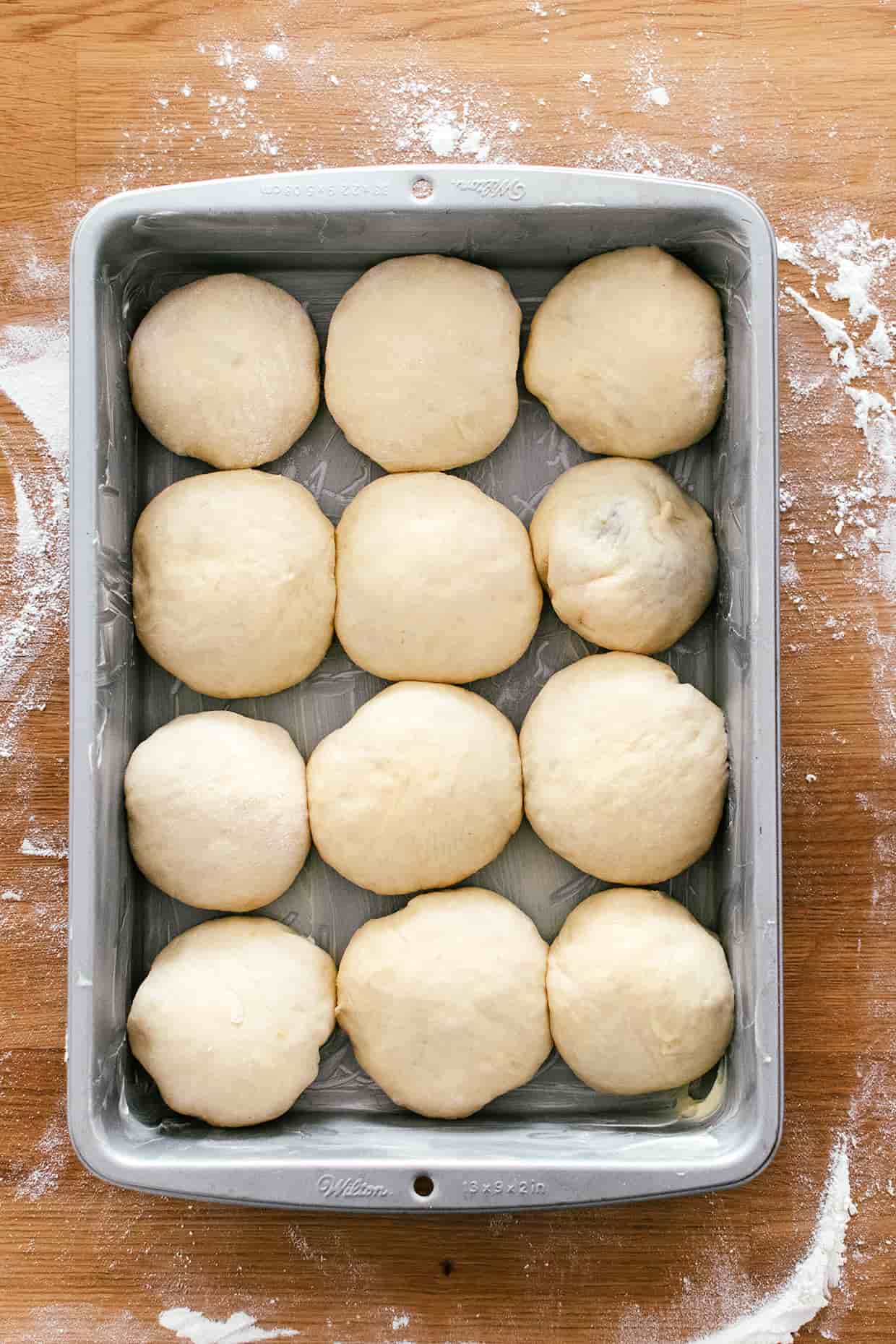 baking pan greased with butter and filled with twelve bread rolls, waiting to rise 
