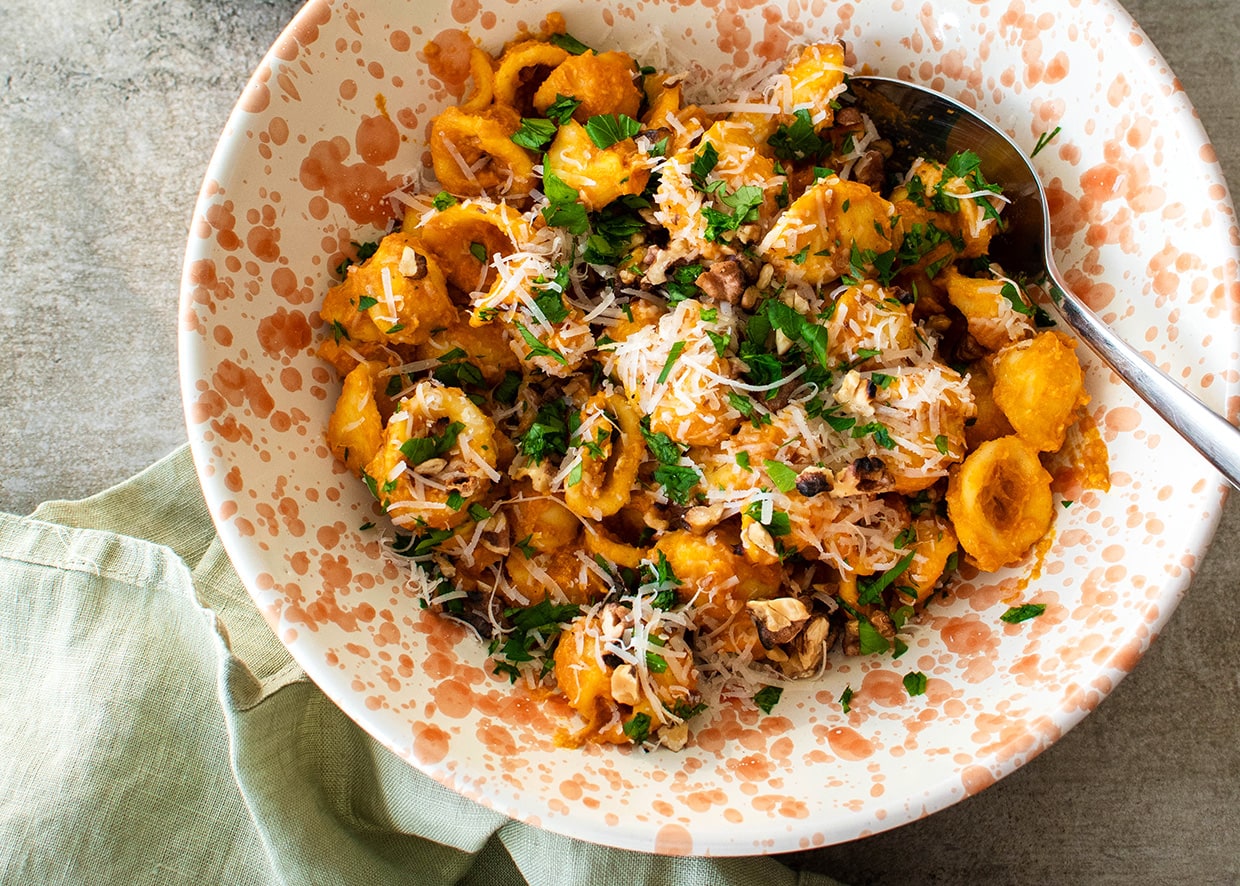 pumpkin sauce pasta served in bowl with cheese, walnuts and parsley