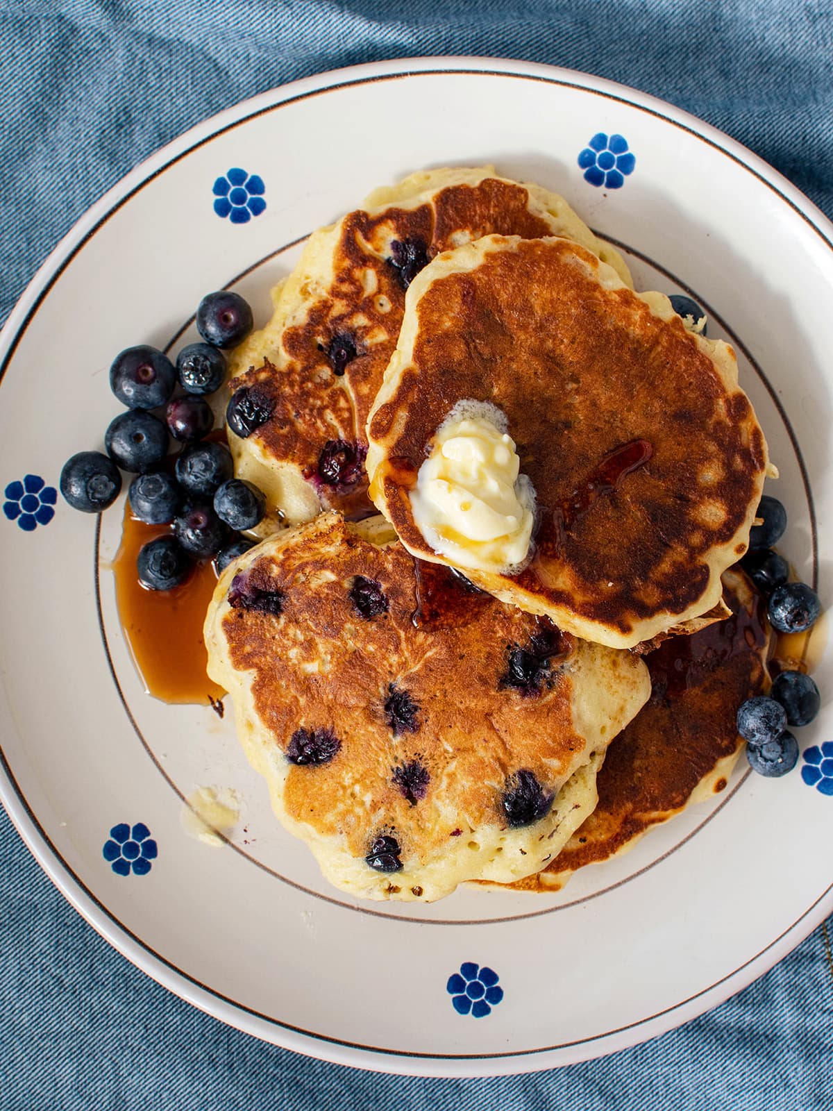 plate with blueberry pancakes topped with butter and maple syrup