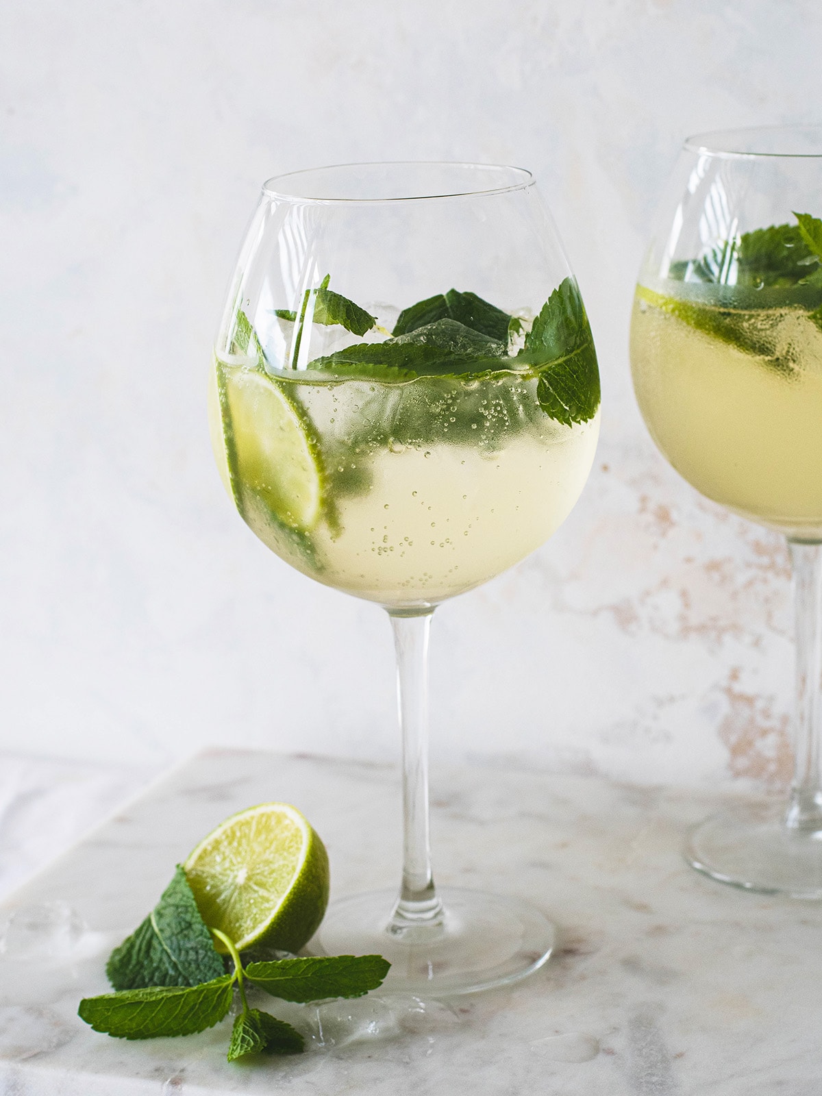 two wine glasses with elderflower spritz, mint and limes