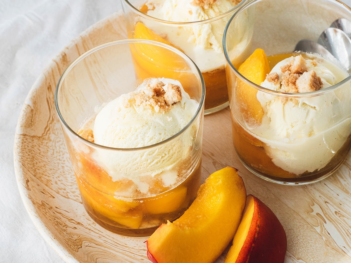glasses with sliced peaches in white wine with ice cream on top