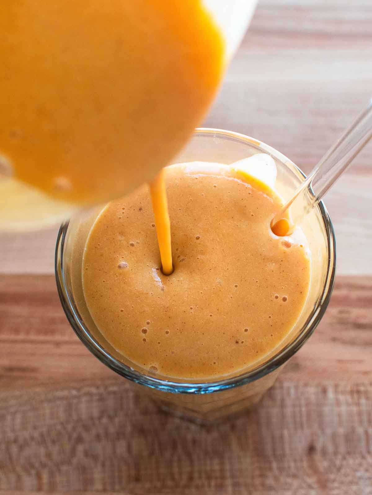 pouring an orange sweet potato smoothie in a glass